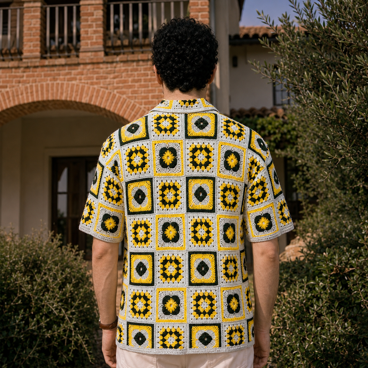 Back view of a man wearing a yellow, black, and gray granny-square crochet shirt